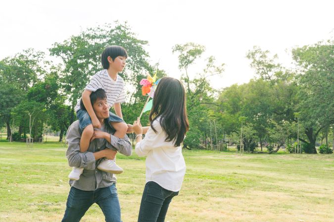 Son sitting on father’s shoulders facing mother in park