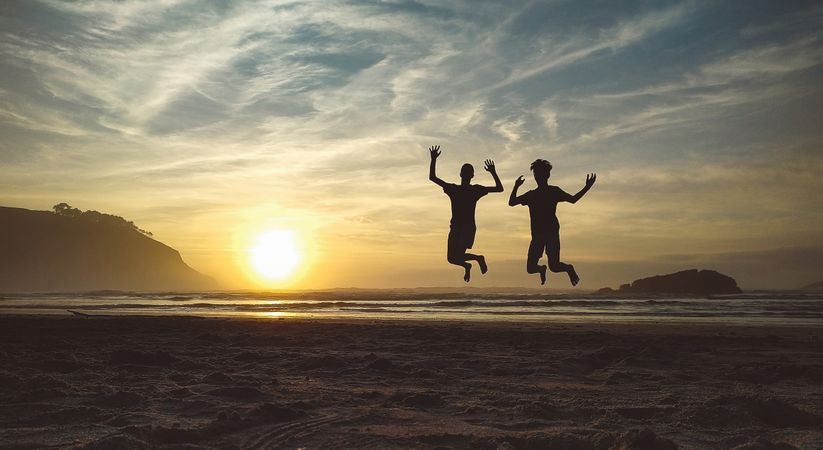Silhouettes of two kids jumping in the beach at sunset