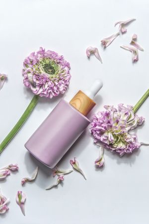 Pastel purple cosmetic bottle with pipette and beautiful flowers and petals