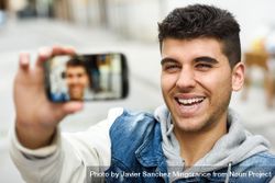 Smiling man in jean jacket taking selfie outside 4Z1YN5