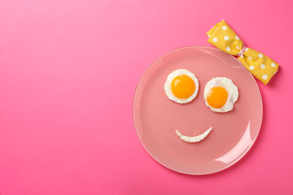 Looking down at pink plate with smiley face on it made of eggs and condiments, copy space