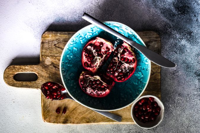 Open pomegranate in teal bowl with knife and spoon
