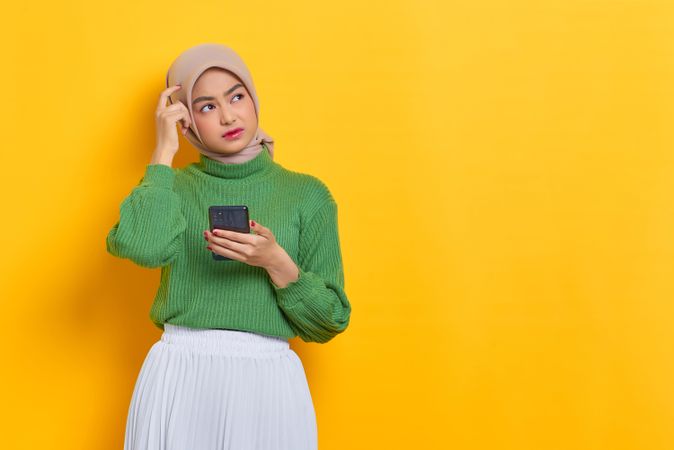 Woman in headscarf scratching head and holding smart phone
