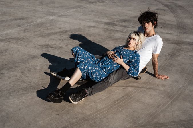 Trendy couple sitting together on skateboard on street