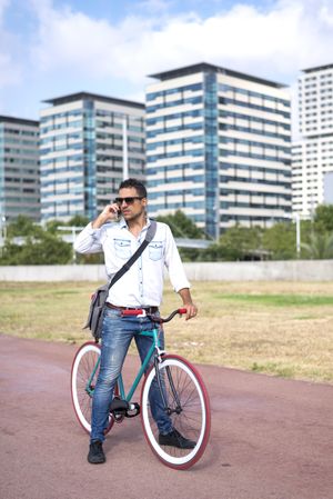 Male with colorful bicycle talking on phone on city bike path, vertical