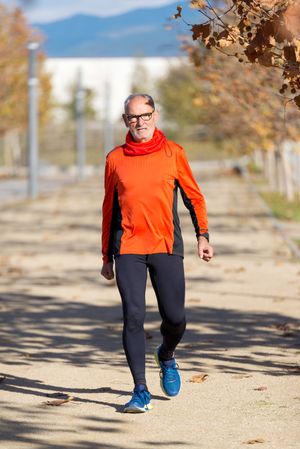 Older man in leggings and windbreaker walking in park