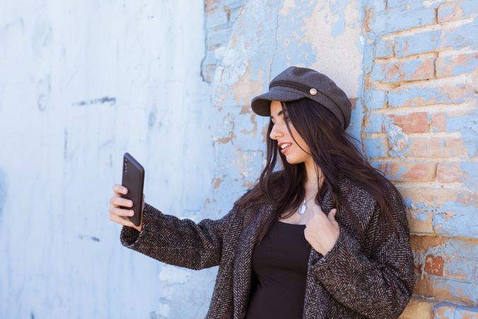 Charming Hispanic lady taking selfie near wall