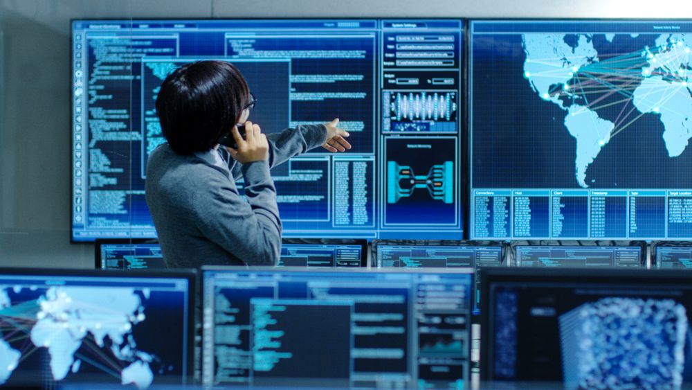 In the System Control Room IT Administrator Talks on the Phone.