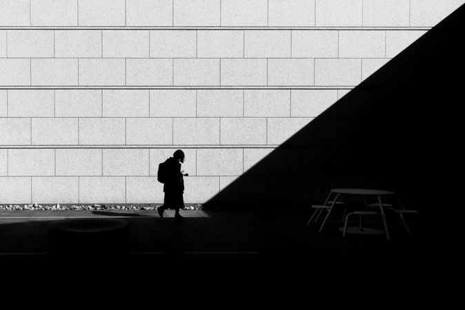 Grayscale photo of person with backpack walking on sidewalk