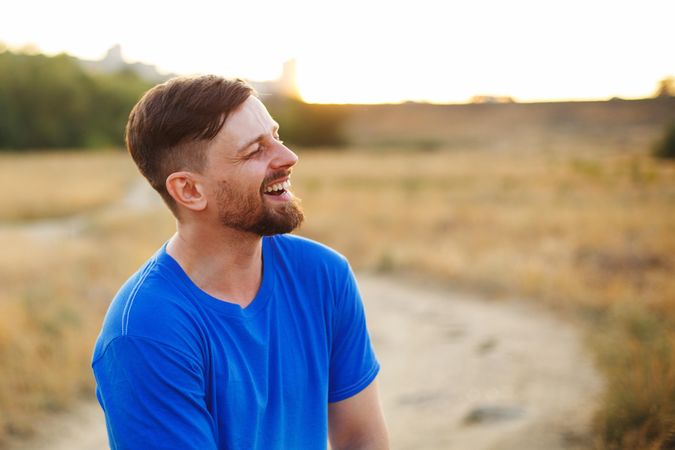 Male in blue t-shirt standing and smiling in long grass field