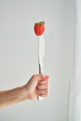 Crop person showing strawberry pricked on knife