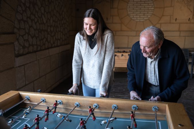 A granddaugther and his grandfather are playing table football game and having fun together