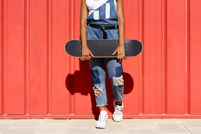 Body of female skater in front of a red wall with skateboard