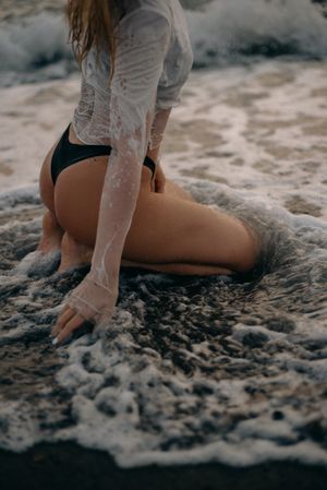 Back view of woman in dark panty and light shirt sitting on beach sand