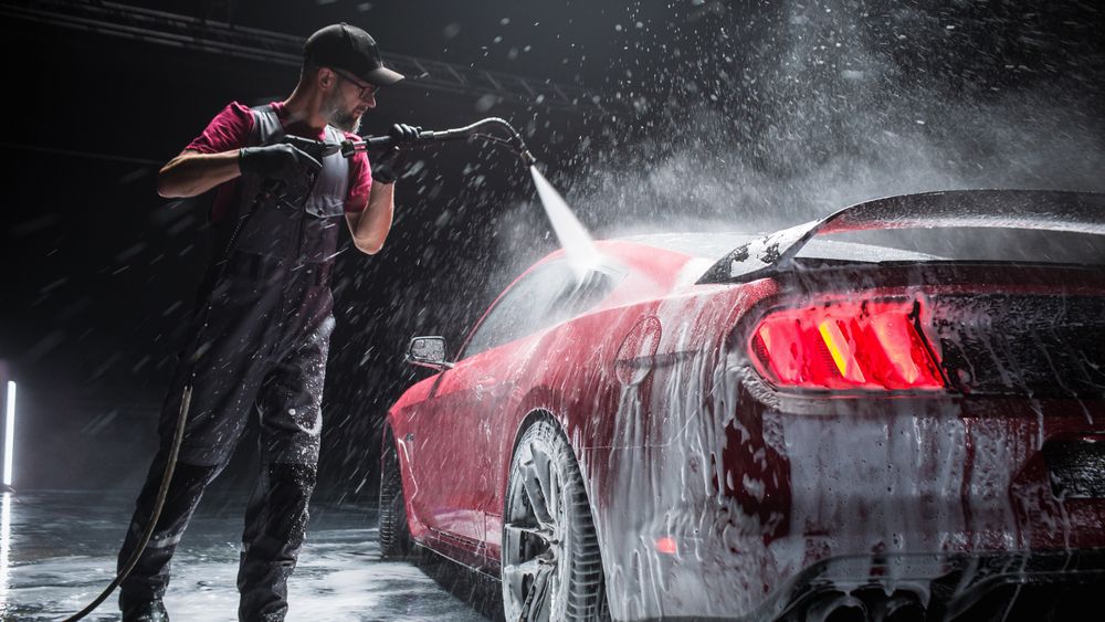 Automotive Detailer Washing Away Smart Soap and Foam with a Water High Pressure Washer.