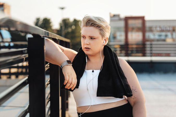 Serious woman in fitness gear leaning on rooftop rail after a workout