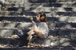 Child sitting on cement steps in outdoor park holding up a autumn leaf