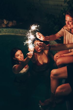 Cheerful friends burning sparkles near pool