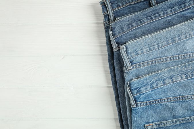 Different jeans folded on a wooden background, space for text