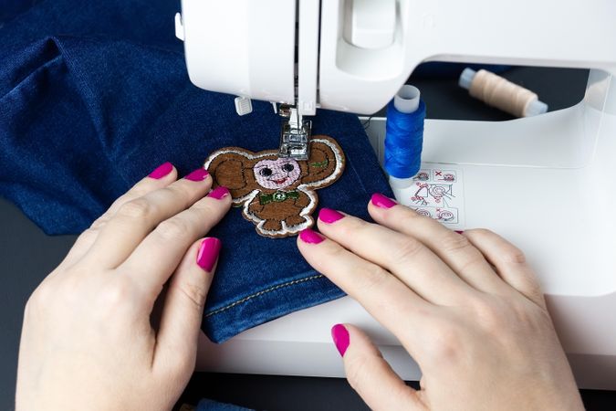 Person sewing badge on jeans pants