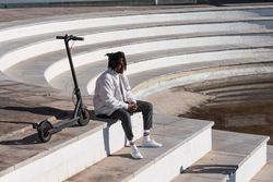 Black hipster man with scooter sitting on steps