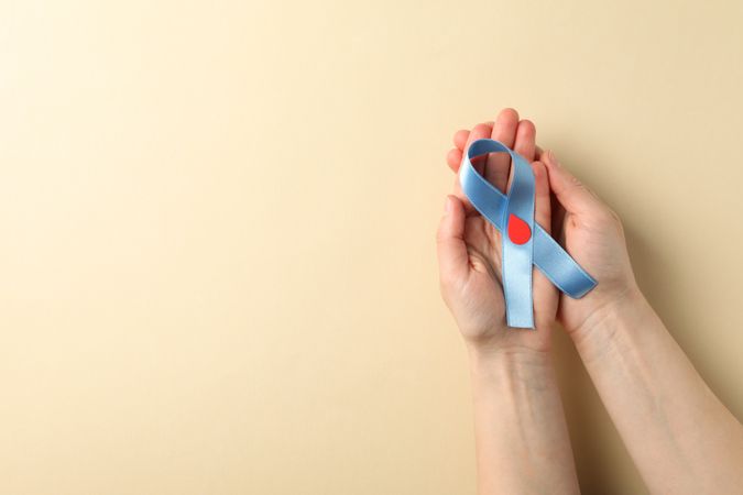 Female hands hold diabetes awareness ribbon on beige background