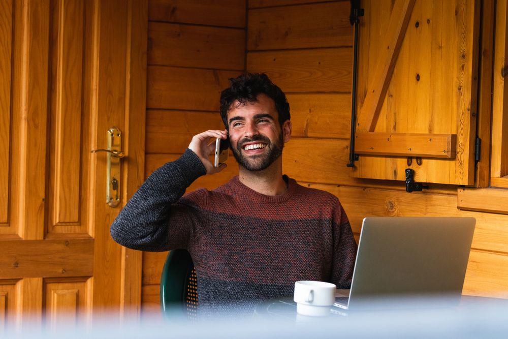 Cheerful man speaking on smartphone and working on terrace