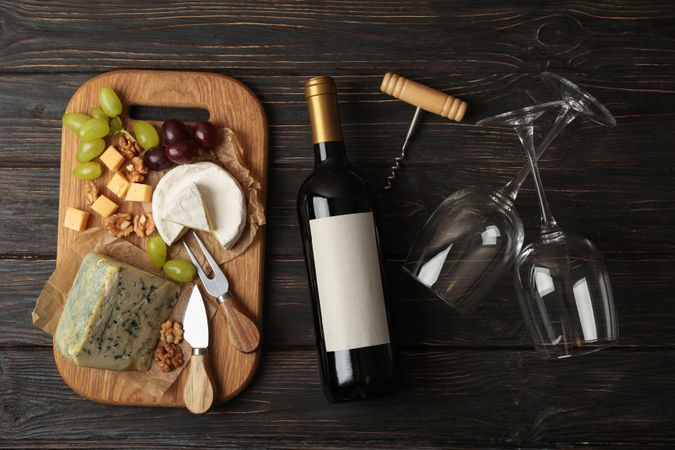 Bottle of wine, glasses, cheese and fruits on wooden background, top view