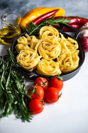 Raw Fettuccine pasta in pan surrounded by fresh vegetables