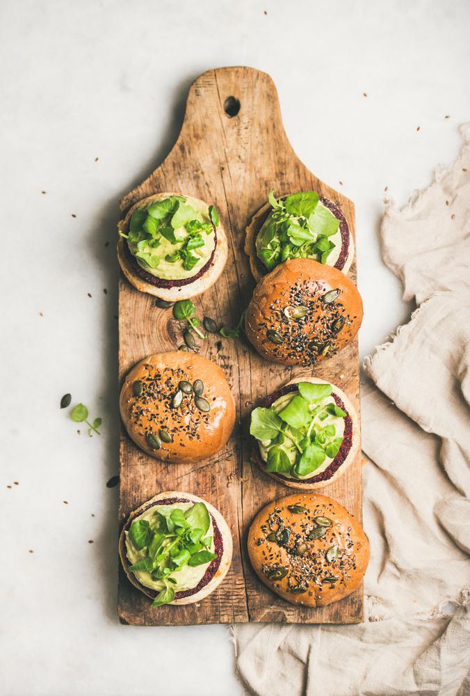 Fresh vegan burgers on seeded buns arranged on wooden bread board