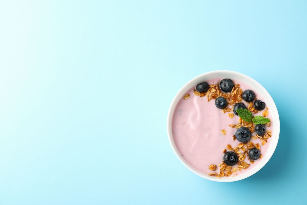 Yogurt with granola, blueberry and mint on color background