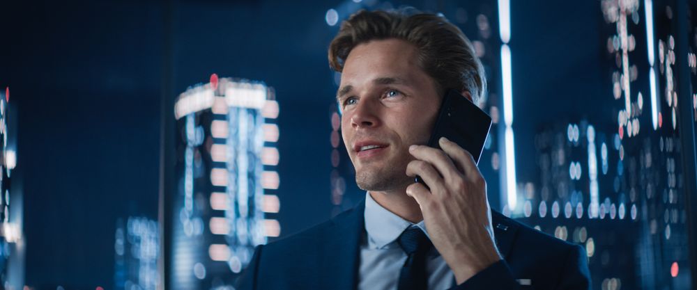 Close Up Portrait of White Businessman in Stylish Suit Standing Next to Window in Big City Office with Skyscrapers Late At Night.
