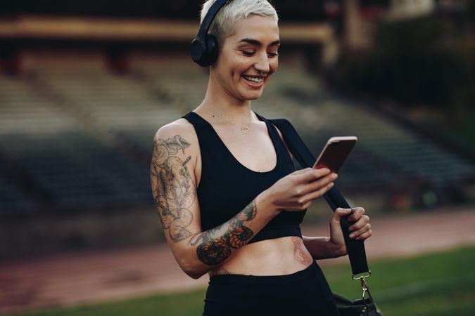 Happy fit woman using mobile phone standing in a track and field stadium