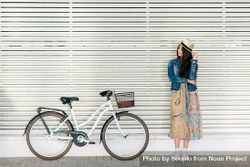 Woman in floral dress leaning on light wall beside light bicycle bedN64