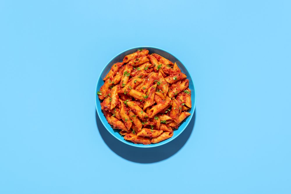 Penne pasta in tomato sauce, top view on a blue background