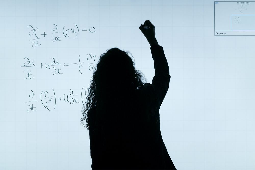 Back view silhouette of a math teacher writing on light board in classroom