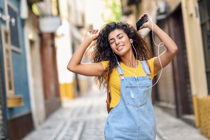Arab woman listening to music with earphones and dancing in lane