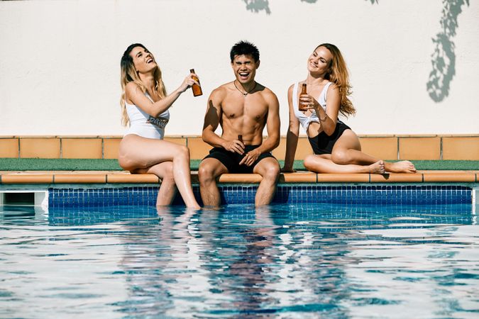 two young women and an asiatic man drinking beer by the pool