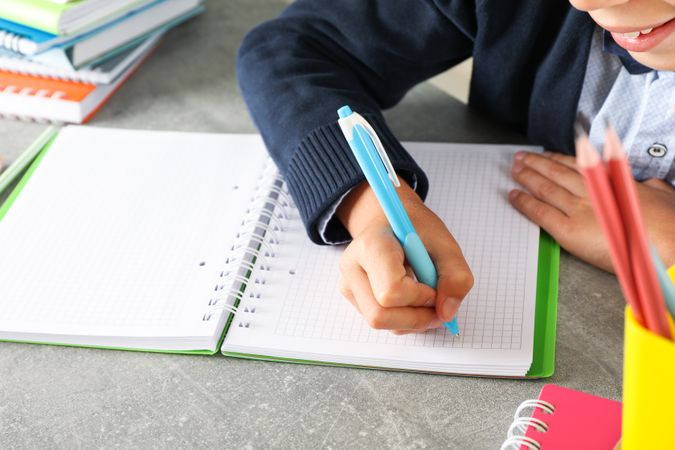 Boy writes in a notebook on grey table, space for text