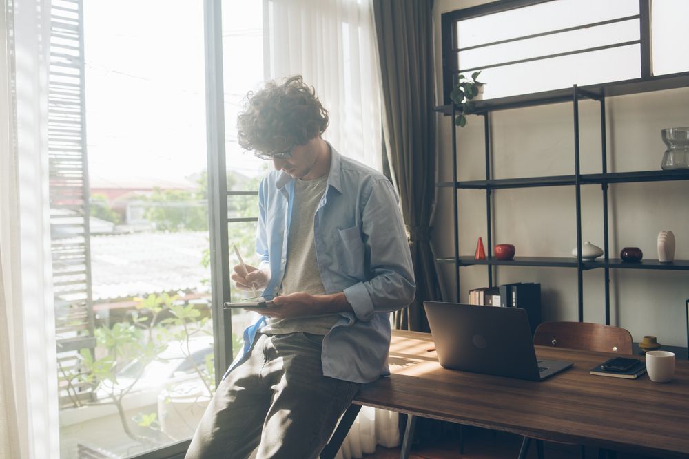 Creative designer writing on digital tablet sitting on desk at home
