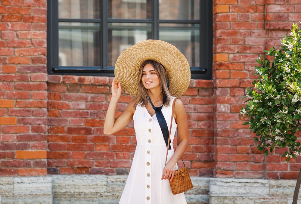 Woman adjusting her straw hat outside a brick building