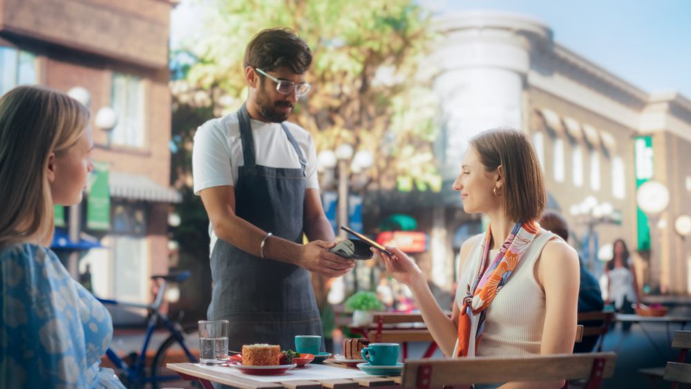 Female is Making a Payment to a Waiter with Her Smartphone.