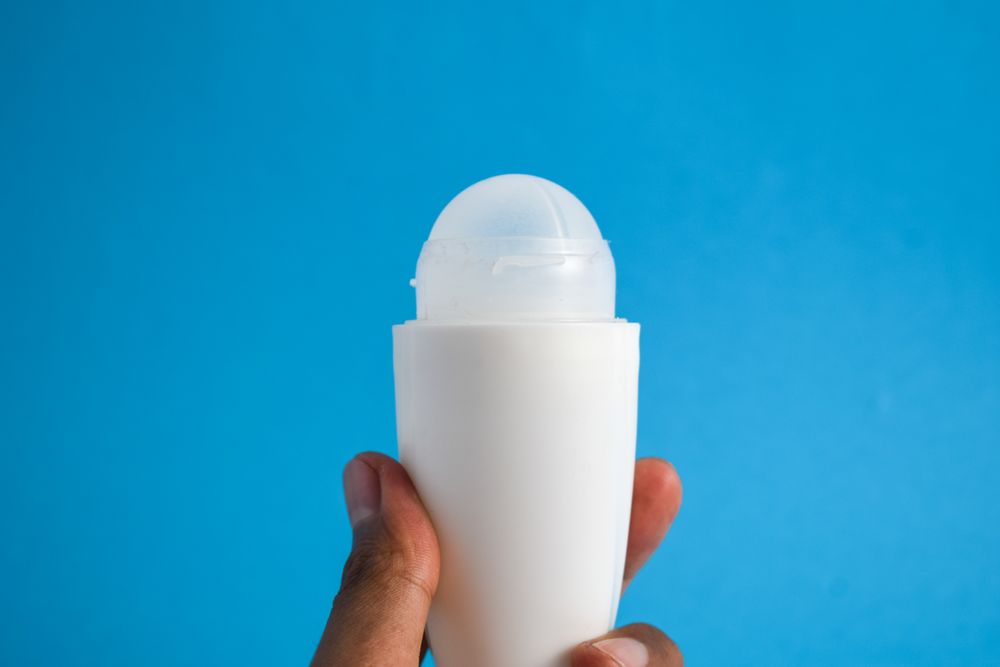 Person holding roller cosmetic bottle on blue background