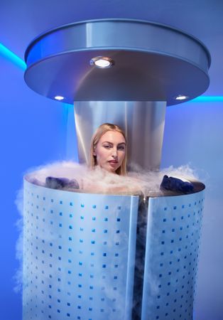 Blonde woman in cryotherapy chamber with steam coming out over the top