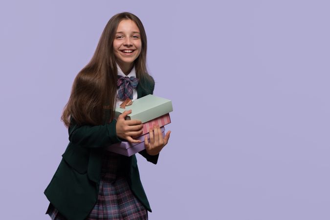 Student in uniform holding colorful gift boxes.