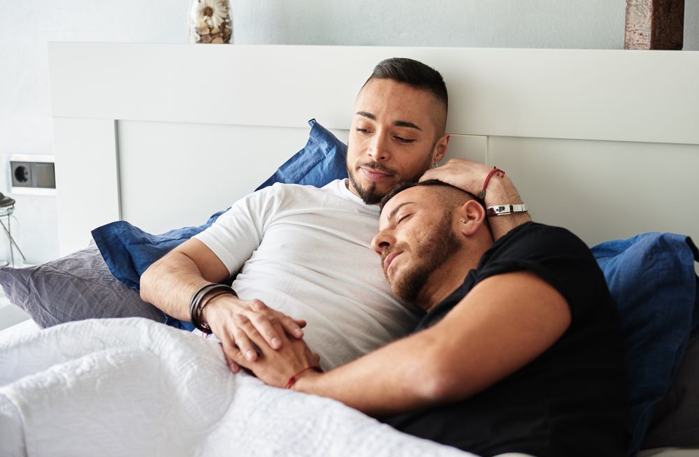 Smiling gay couple hugging on bed