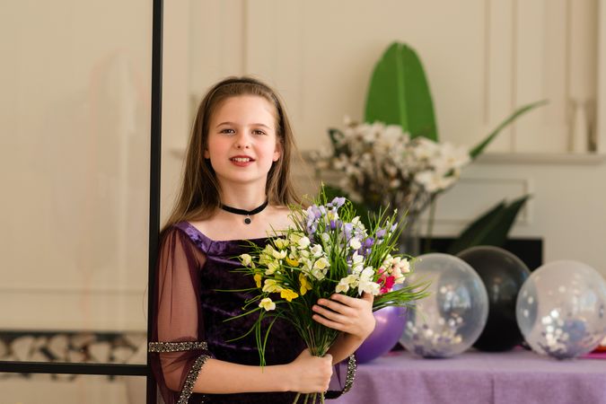 Girl holding bouquet of flowers and smiling at birthday party.
