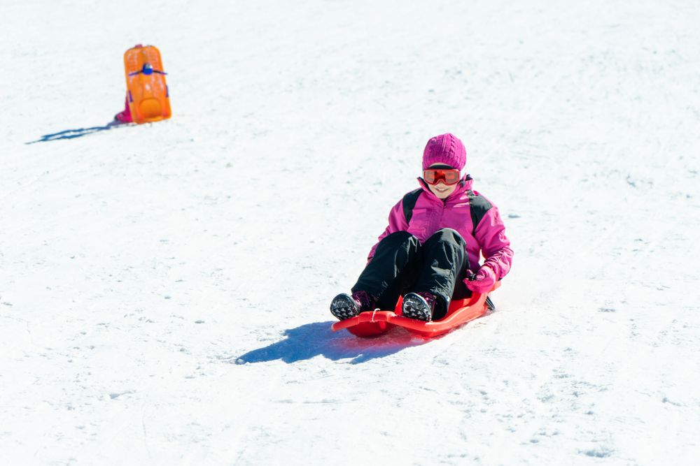 Child in pink snow suit going down a snowy hill in a red sled