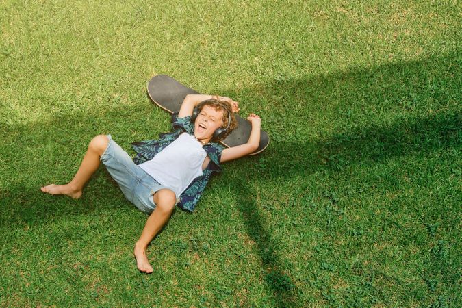 Boy screaming and lying on skateboard on grass
