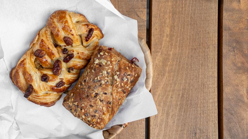 Fresh baked breakfast pastries pecan danish multigrain croissant on paper wooden background